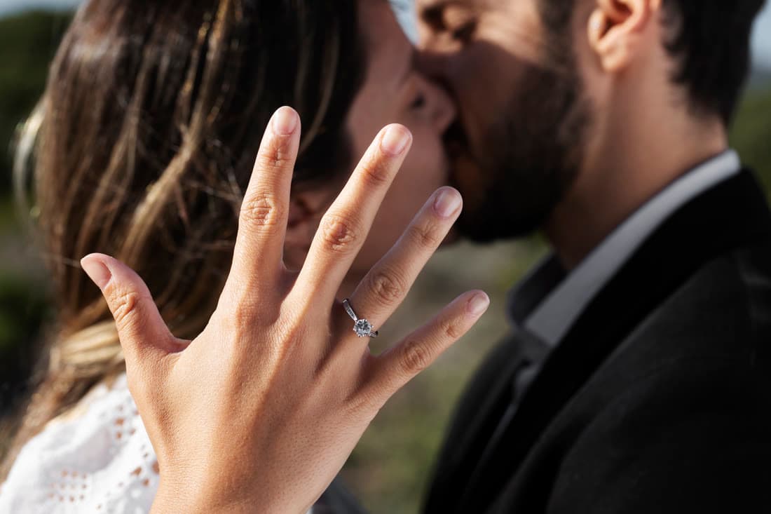 A newly engaged couple laughing as she shows the ring to friends