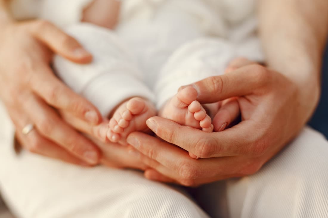 A father holding his newborn against his chest in a chair by the window