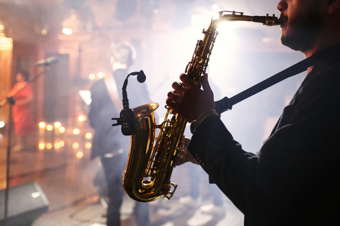 A saxophonist playing with his band on a small stage lit from behind