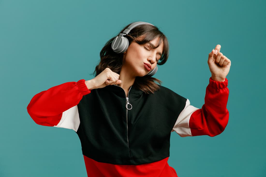 A woman dancing with headphones on against a bright teal background