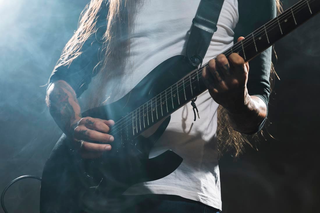 A long-haired guitarist playing an electric guitar in stage smoke
